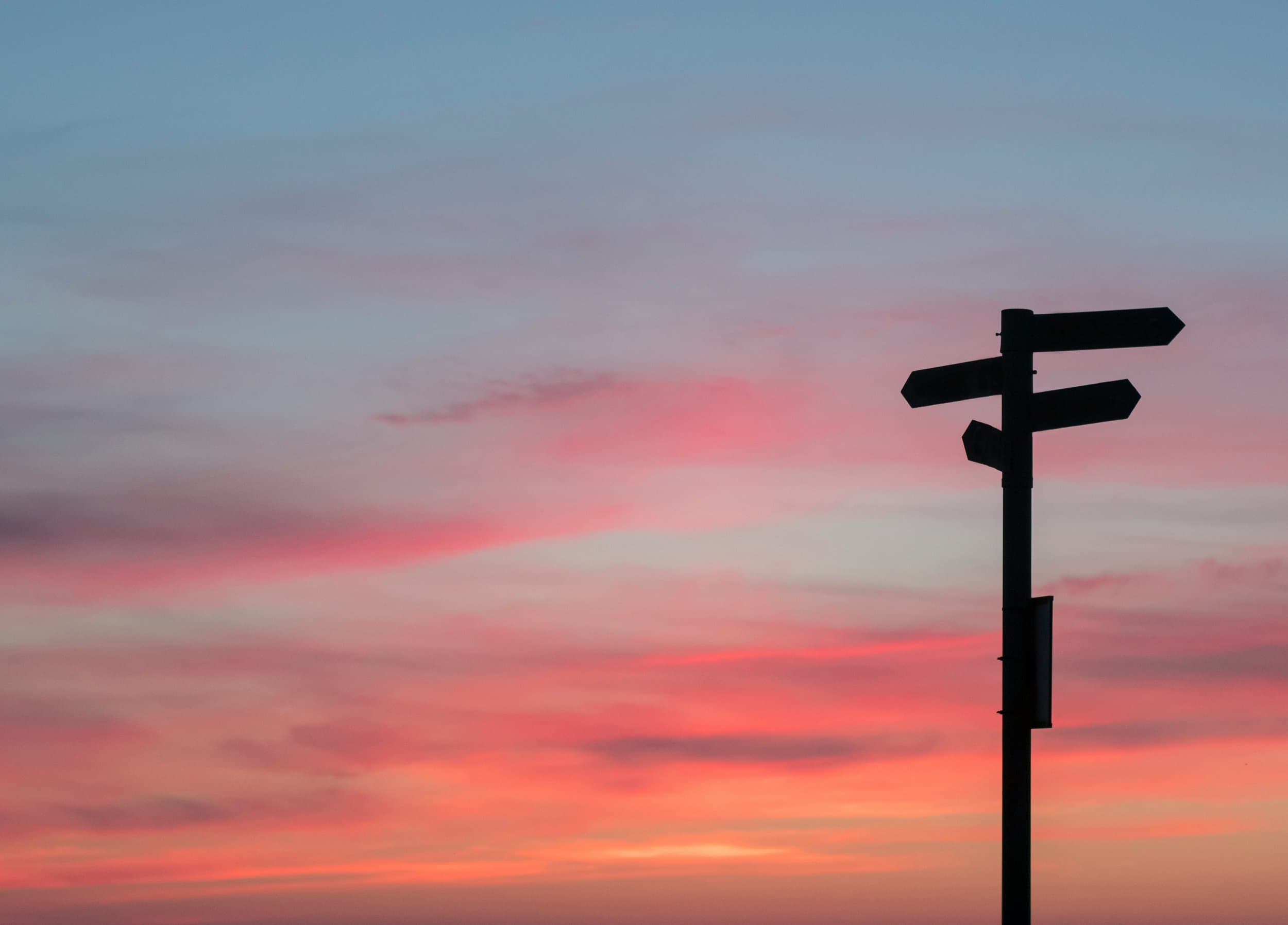 A signpost silhouetted against a pink and purple sky.